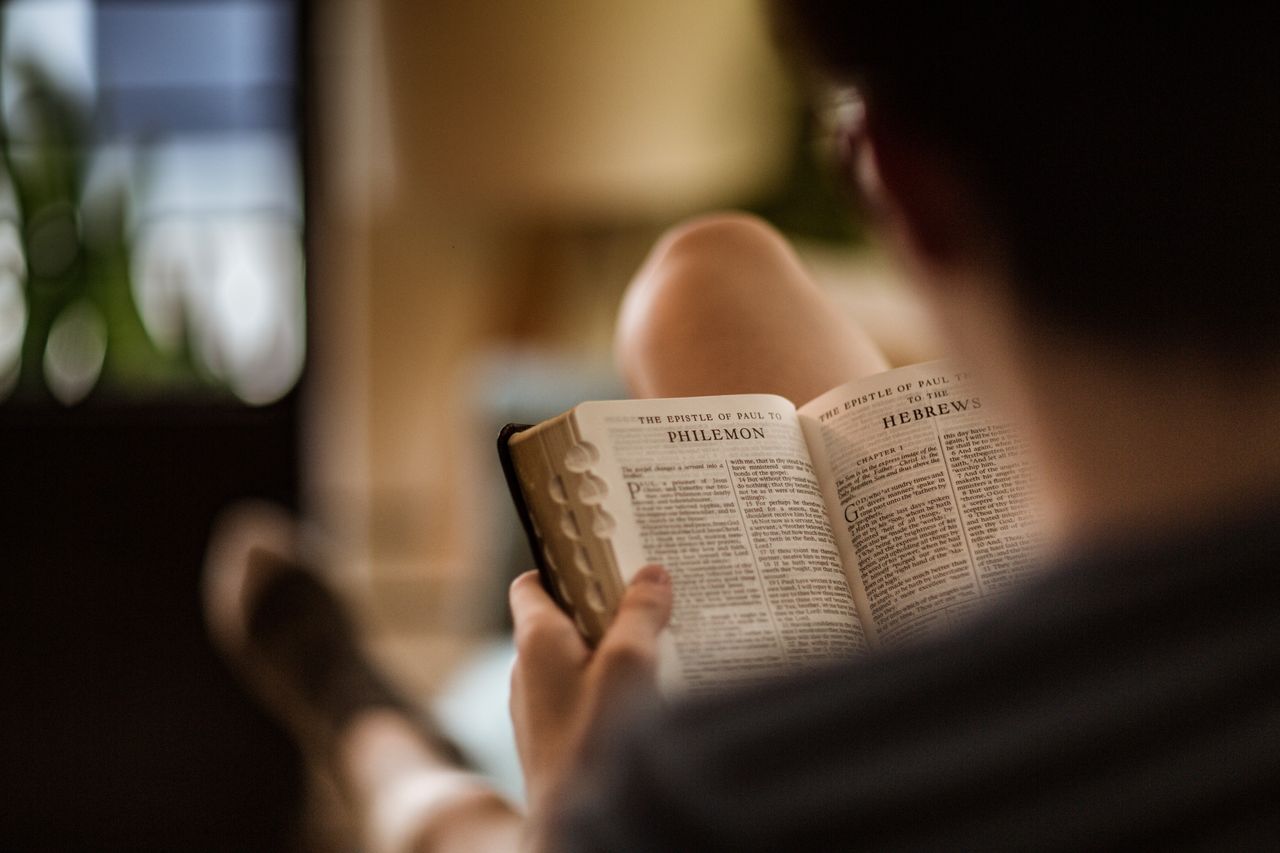 Mężczyzna siedzący na kanapie studiuje Biblię, która jest otwarta na stronach Listu Pawła do Filemona